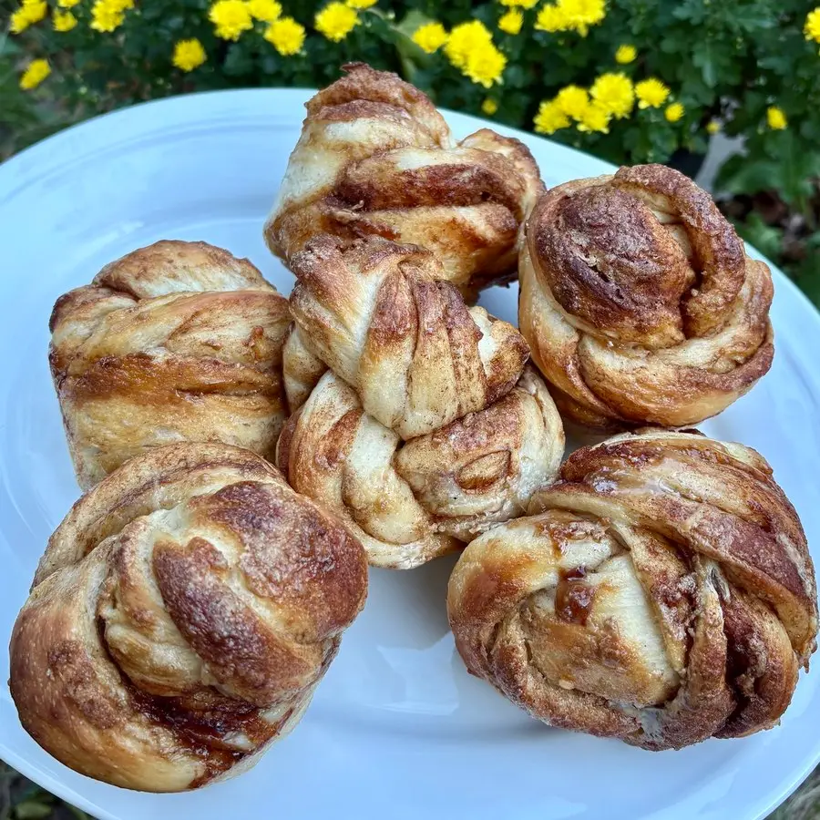 Six personal-sized cinnamon swirl loaves, each the size of a jumbo muffin, on a white plate in front of yellow mums