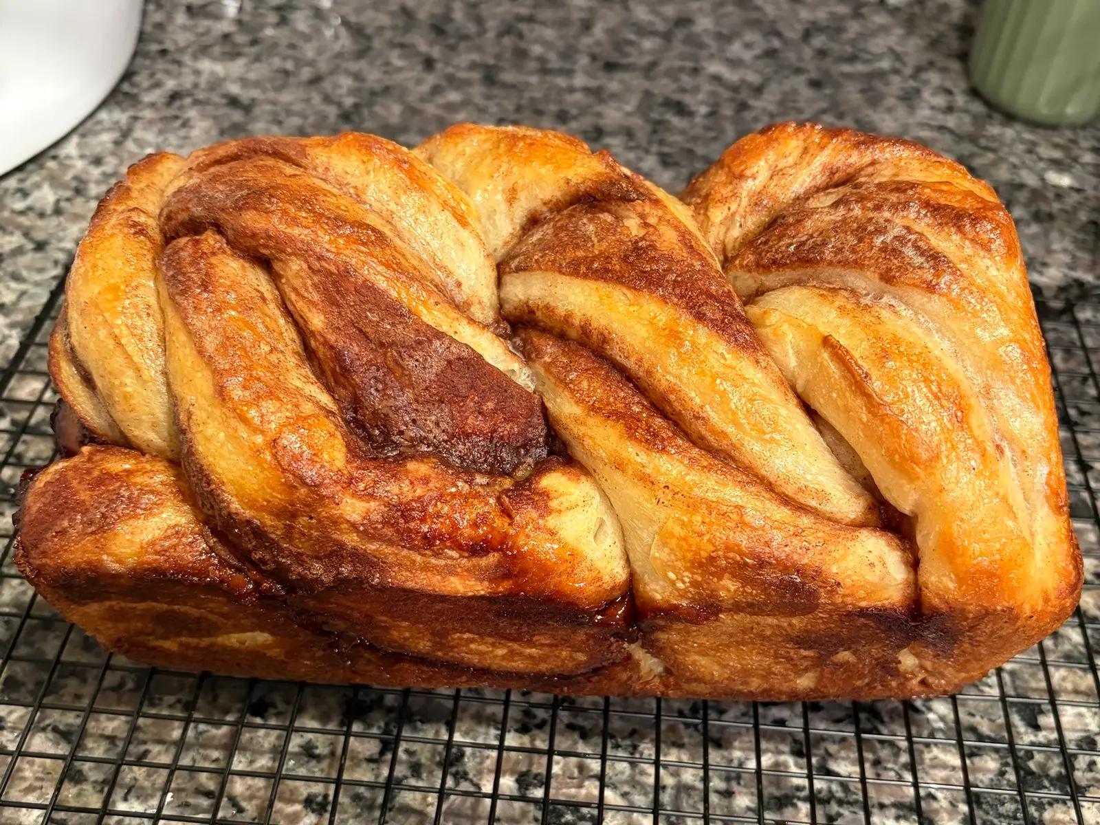 A braided cinnamon swirl sourdough loaf on a cooling rack, ribbons of caramelized cinnamon sugar running through its golden top