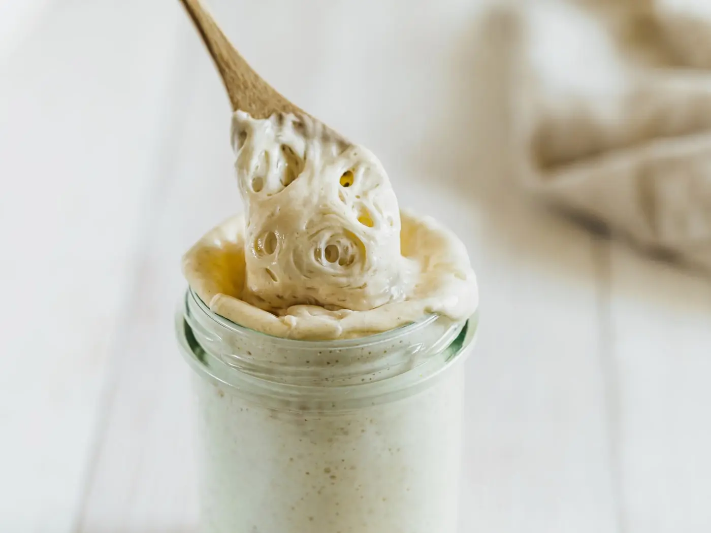 A sourdough starter being lifted from its jar on a wooden spoon